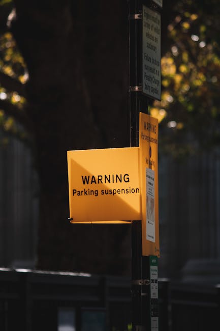 A yellow warning sign attached to a metal pole indicates parking suspension for house removals in Kingston upon Thames, with the sign displaying the message 'WARNING Parking suspension.' The sign is l